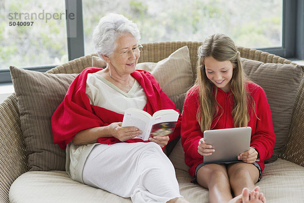 Seniorin beim Lesen einer Zeitschrift mit ihrer Enkelin auf einem digitalen Tablett