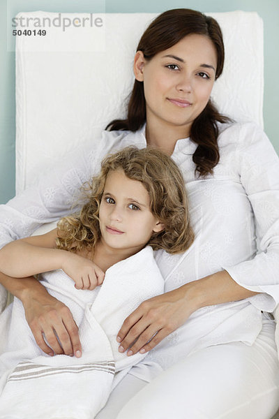 Porträt einer jungen Frau  die mit ihrer Tochter in weißes Handtuch gehüllt liegt.