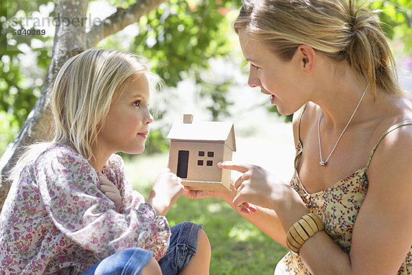 Kleines Mädchen und ihre Mutter halten ein Puppenhaus im Freien.