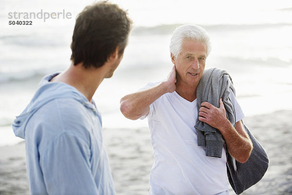 Ein älterer Mann spricht mit seinem Sohn am Strand.