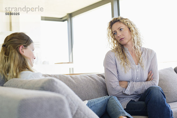 Mittlere erwachsene Frau  die ihre Tochter auf einer Couch sitzend ansieht.