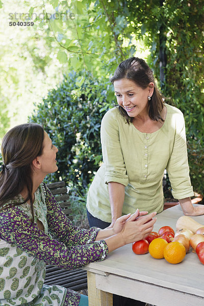 Seniorin im Gespräch mit ihrer Tochter mit Gemüse auf dem Tisch