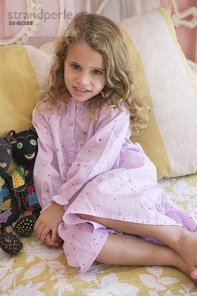 Porträt eines kleinen Mädchens auf dem Bett sitzend
