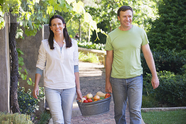 Ein reifes Paar  das einen Früchtekorb im Garten trägt.