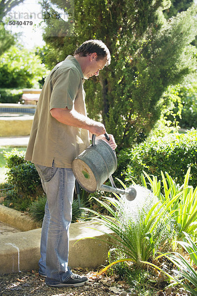 Seitenprofil eines reifen Mannes beim Gießen von Pflanzen in einem Garten