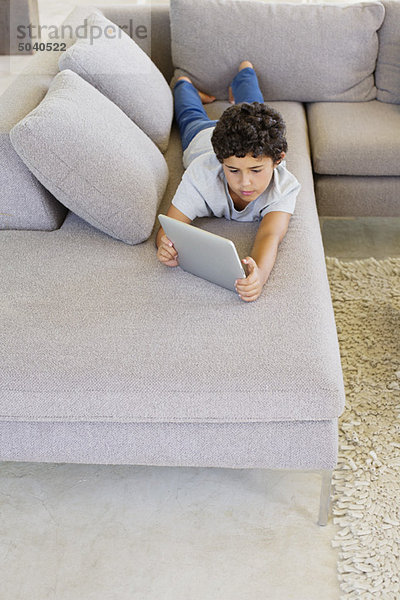 Junge  der auf einer Couch liegt und ein digitales Tablett benutzt.