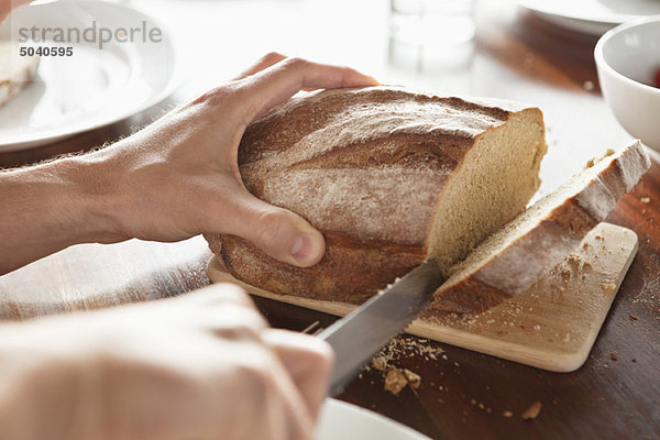 Nahaufnahme der Hand eines Menschen beim Brotschneiden