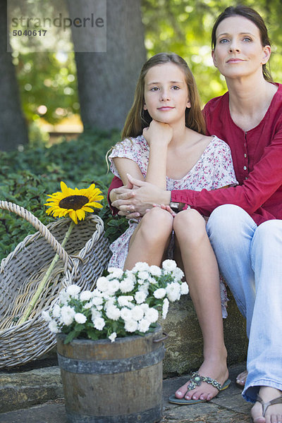 Kleines Mädchen und Mutter sitzend im Freien mit Blumen im Korb