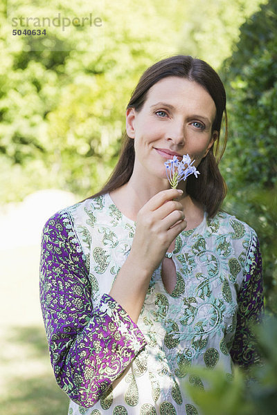 Porträt einer lächelnden  reifen Frau  die im Garten Blumen riecht.