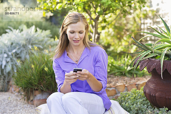 Schöne junge Frau SMS im Garten