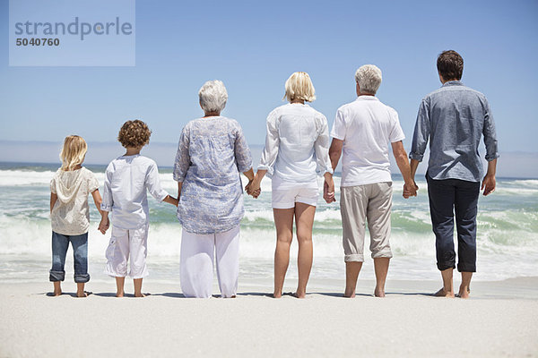 Rückansicht einer Familie mit Blick vom Strand auf das Meer