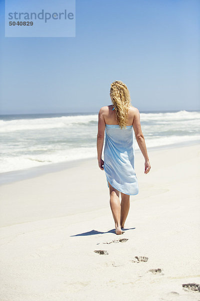 Rückansicht einer am Strand spazierenden Frau