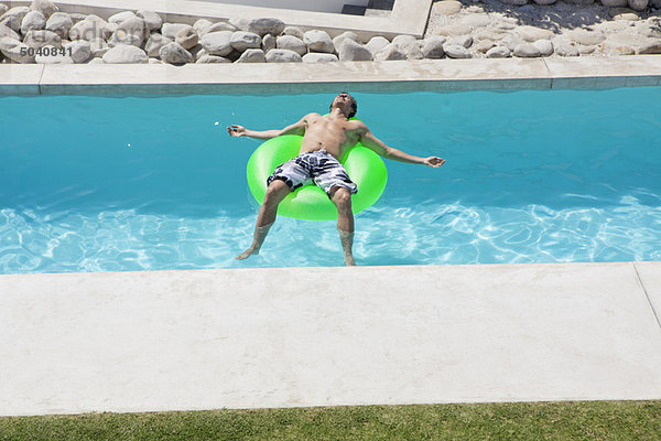 Mann entspannt auf einem aufblasbaren Ring im Pool