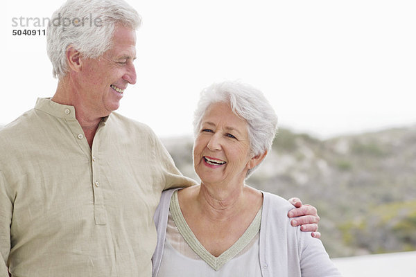 Älterer Mann steht mit dem Arm um eine ältere Frau.