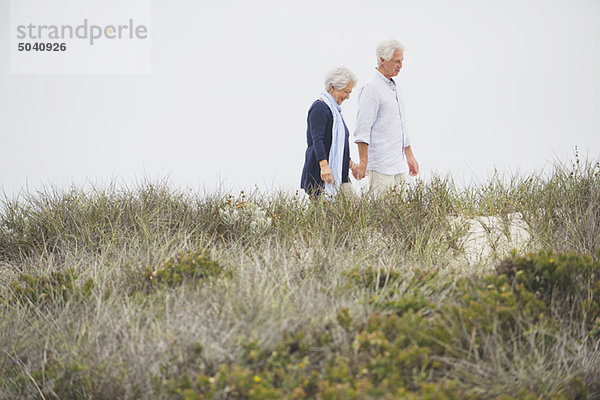 Seniorenpaar  das am Strand spazieren geht und sich an den Händen hält.