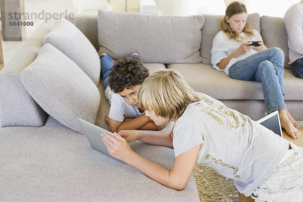 Teenager-Junge mit seinem Bruder  der ein digitales Tablett benutzt  und seiner Schwester  die im Hintergrund ein Videospiel spielt.