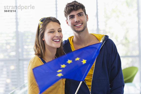 Porträt eines Ehepaares  das auf einem Flughafen die Flagge der Europäischen Union hält.