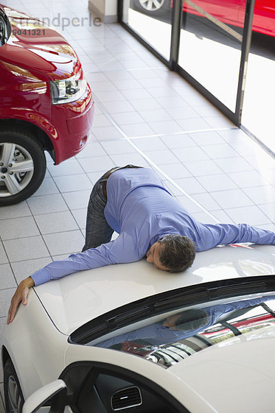 Mittlerer Erwachsener Mann  der die Motorhaube eines Autos umarmt.