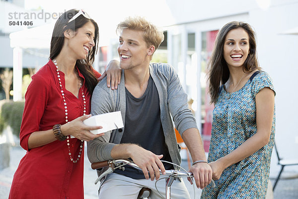 Lächelnder junger Mann mit zwei Frauen beim Radfahren