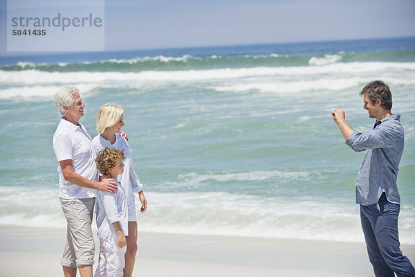 Mittlerer erwachsener Mann beim Fotografieren seiner Familie am Strand