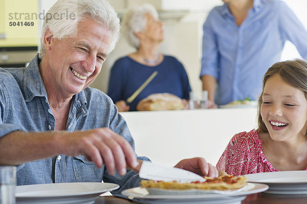 Mann schneidet Kuchen mit einem Messer und seine Enkelin sitzt neben ihm.