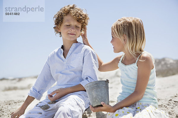 Mädchen hält die Muschel an das Ohr ihres Bruders am Strand.