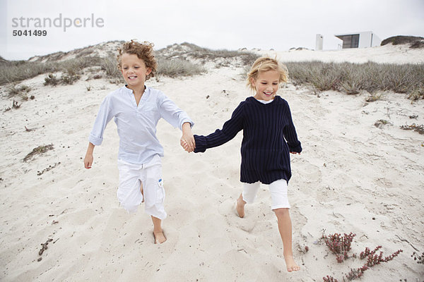 Junge mit seiner Schwester beim Händchenhalten und Laufen auf Sand
