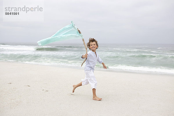 Junge läuft  während er die Fahne am Strand hält