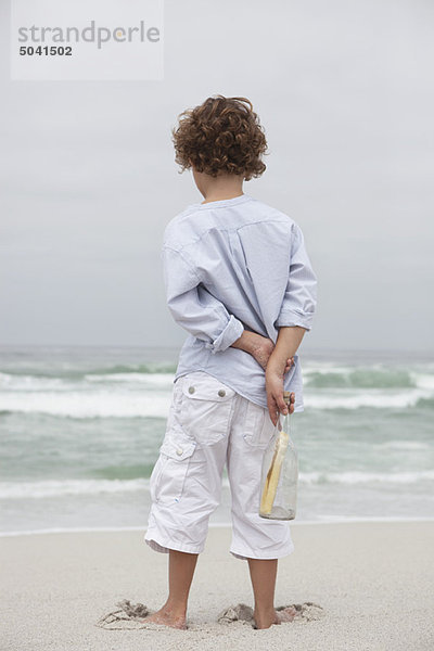 Rückansicht eines Jungen mit Flasche und Botschaft am Strand