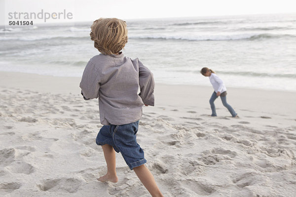 Rückansicht eines Jungen  der mit seiner Schwester am Strand rennt.