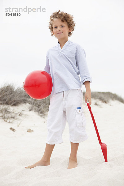 Junge mit Spielzeugschaufel und Ball am Strand