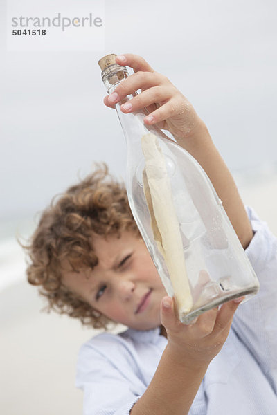 Junge schaut sich die Nachricht in einer Flasche am Strand an.
