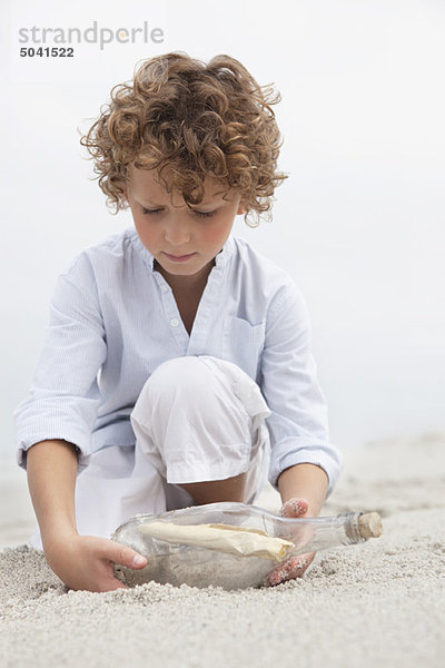 Süßer Junge  der sich die Nachricht in einer Flasche am Strand ansieht.