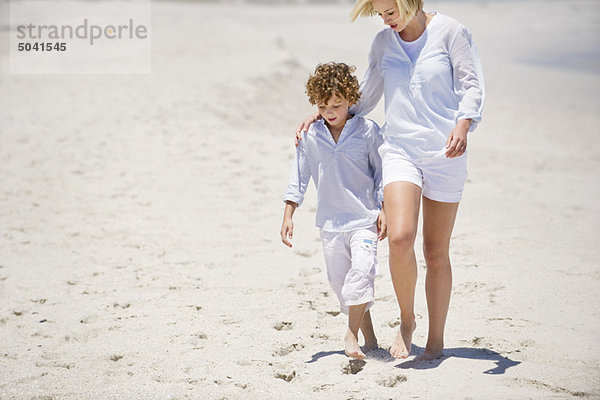 Frau  die mit ihrem Sohn am Strand spazieren geht.