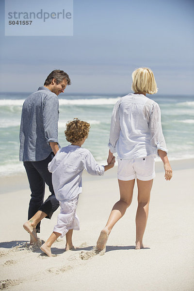 Rückansicht eines Paares  das mit seinem Sohn am Strand spazieren geht.