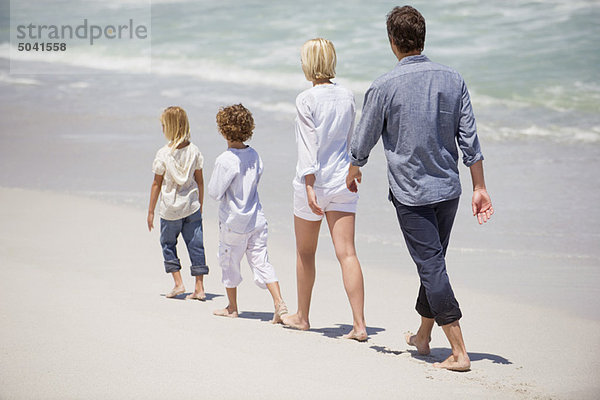 Paar mit zwei Kindern  die am Strand spazieren gehen