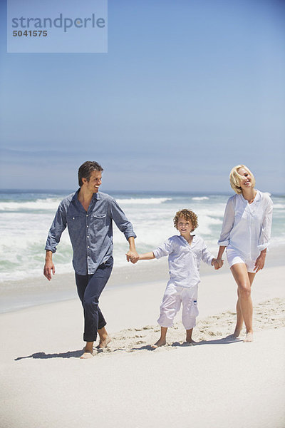 Junge  der mit seinen Eltern am Strand spazieren geht.