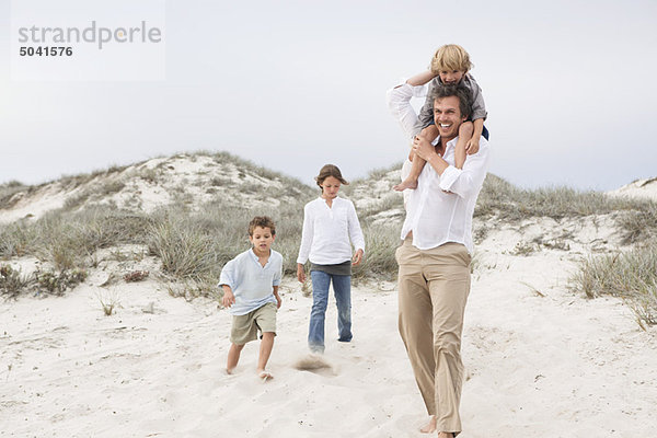 Ein Mann  der mit seinen Kindern auf Sand geht.