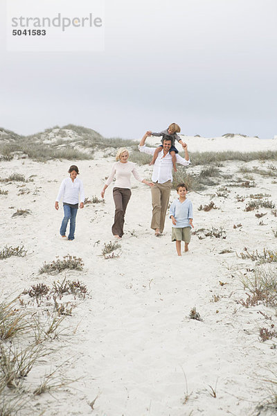 Ein Paar  das mit seinen Kindern am Strand spazieren geht.