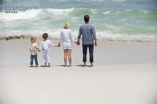 Paar mit zwei Kindern am Strand stehend