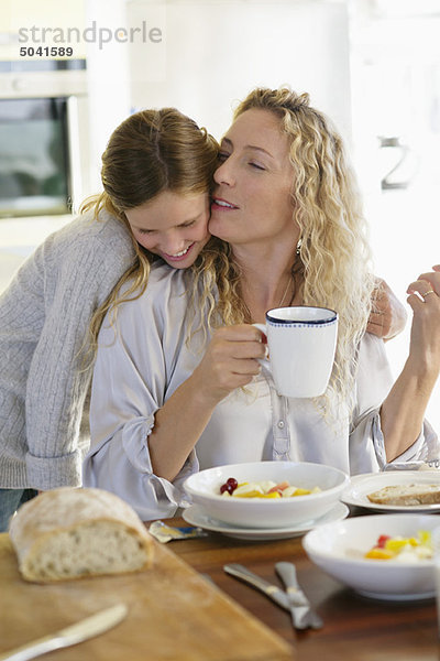 Mittlere erwachsene Frau  die ihre Tochter am Esstisch küsst.