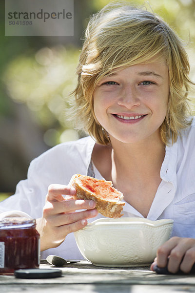 Porträt eines kleinen Jungen  der im Freien Brot mit Marmelade isst.