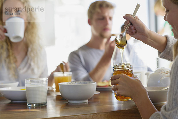 Familienfrühstück zu Hause mit Fokus auf ein Mädchen  das Honig mitnimmt.