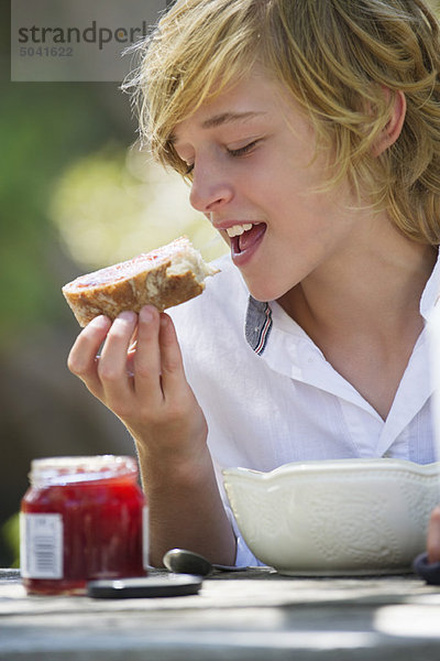 Kleiner Junge isst Brot mit Marmelade im Freien