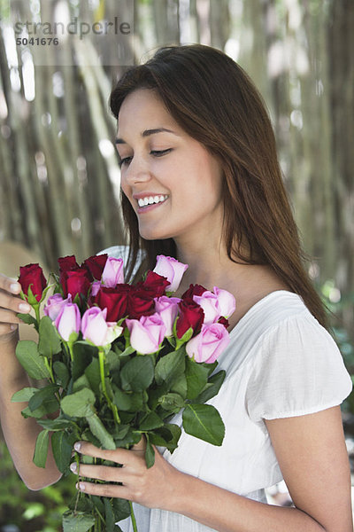 Fröhliche junge Frau schaut auf einen Strauß bunter Rosen.