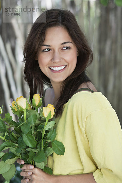 Junge Frau hält gelben Blumenstrauß und lächelt