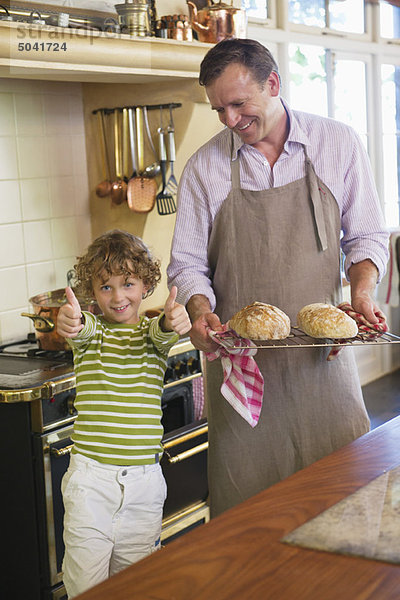 Kleiner Junge mit Daumen nach oben und Vater mit gebackenem Brot.
