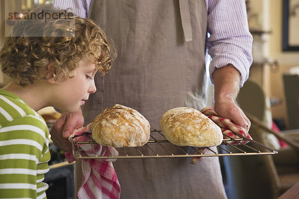 Süßer kleiner Junge  der gebackenes Brot in Vaters Hand riecht.