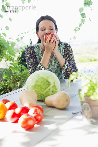 Reife Frau isst Tomate mit Gemüse auf dem Tisch