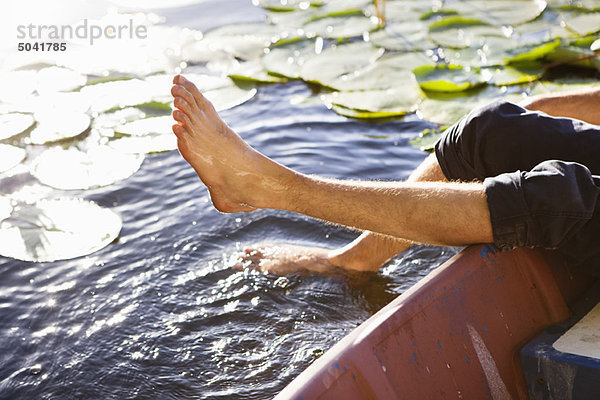 Mann liegt in einem Boot und taucht seine Beine in einen Teich.
